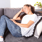 Woman relaxing on a couch with a backrest pillow featuring white patterns.