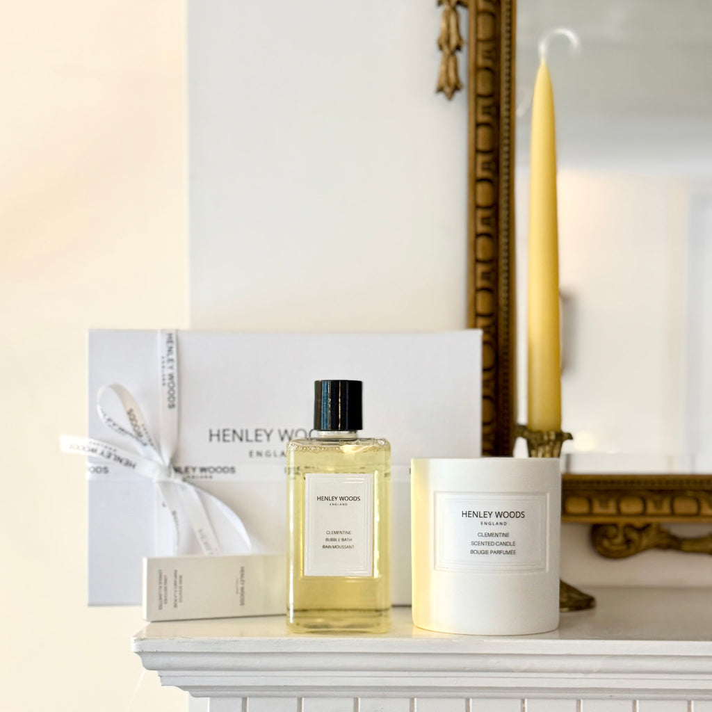 Henley Wood perfume bottle and candle on a white surface with a mirror and yellow candle in the background.