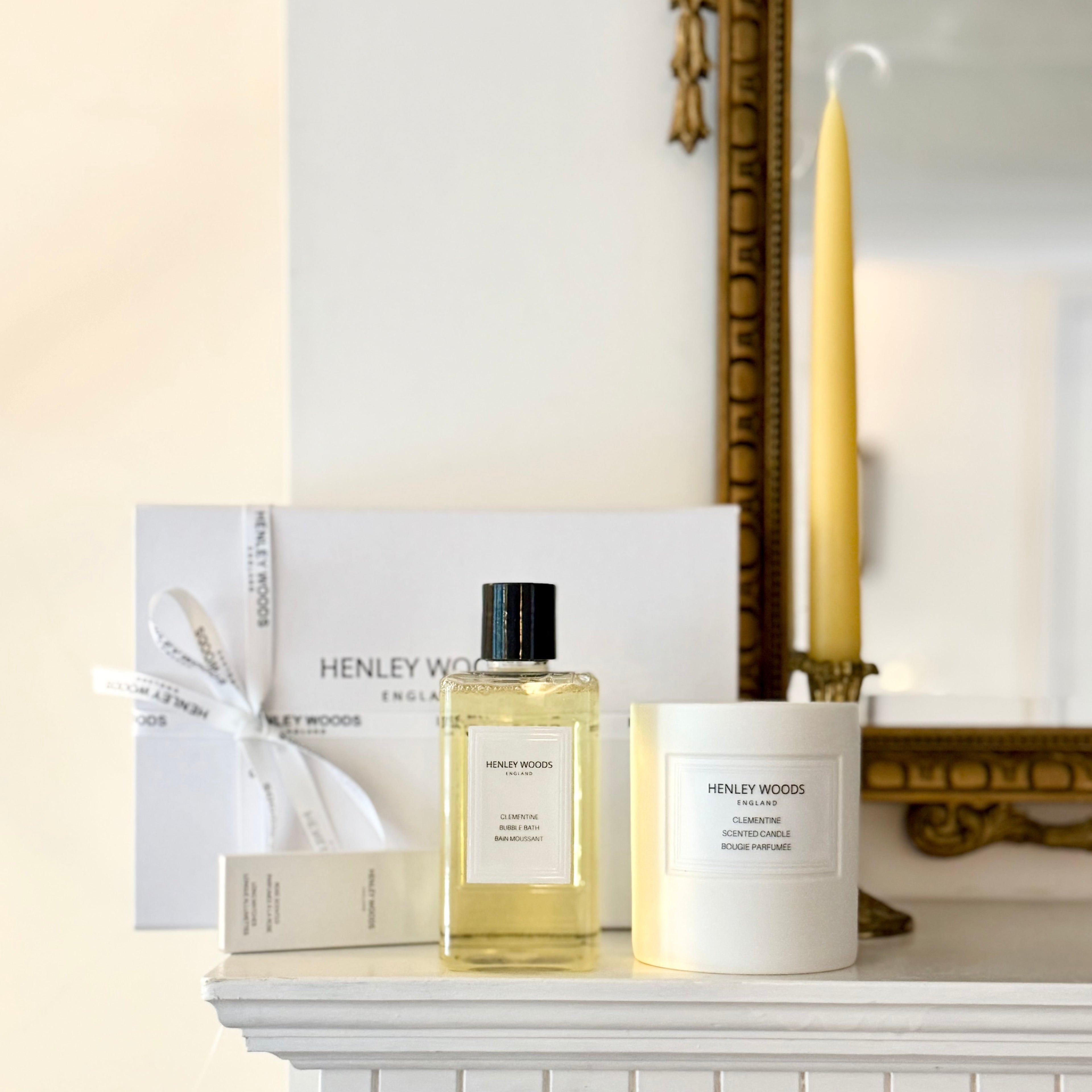 Henley Wood perfume bottle and candle on a white surface with a mirror and yellow candle in the background.