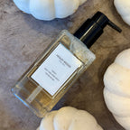 Glass bottle with pump dispenser on a wooden surface with white pumpkins.