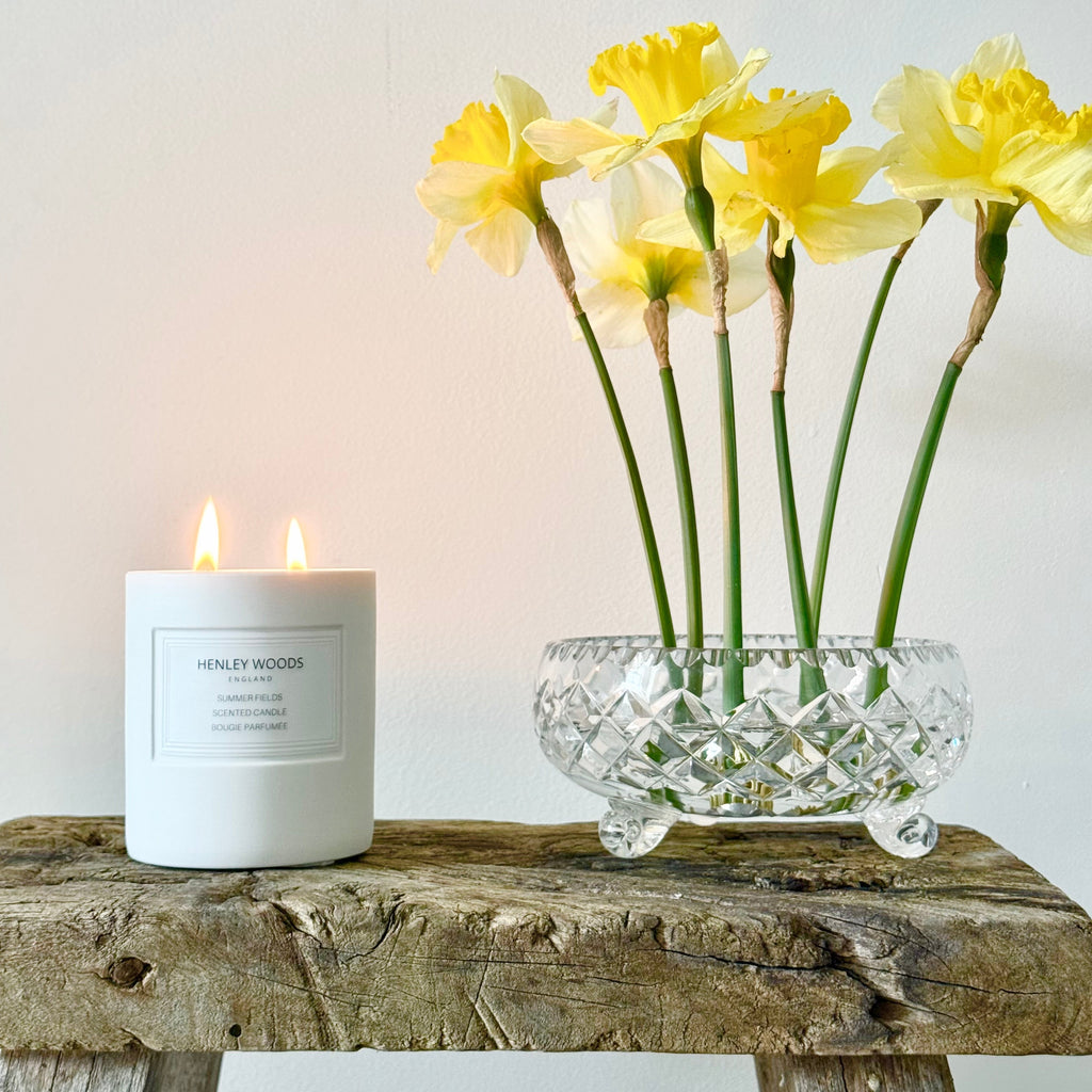 White candle and glass vase with yellow flowers on a wooden surface