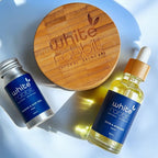 White Rabbit skincare products including a wooden disc, small tube, and bottle on a light blue background.