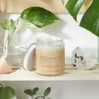 Candle labeled 'Better Me Organics' on a shelf with plants and crystals