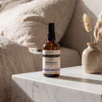 Bottle of Kloris Co soothing mist on a marble surface with a vase and pillows in the background