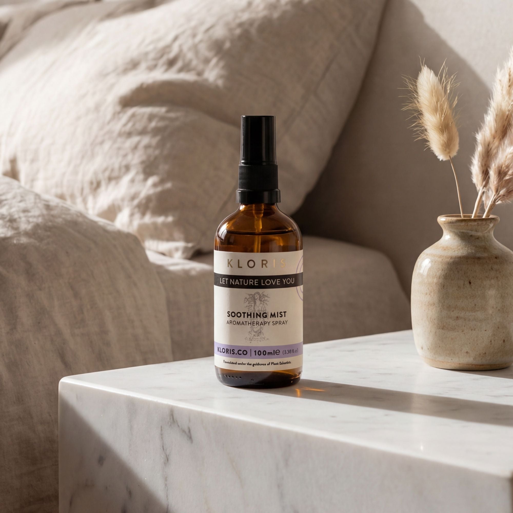 Bottle of Kloris Co soothing mist on a marble surface with a vase and pillows in the background