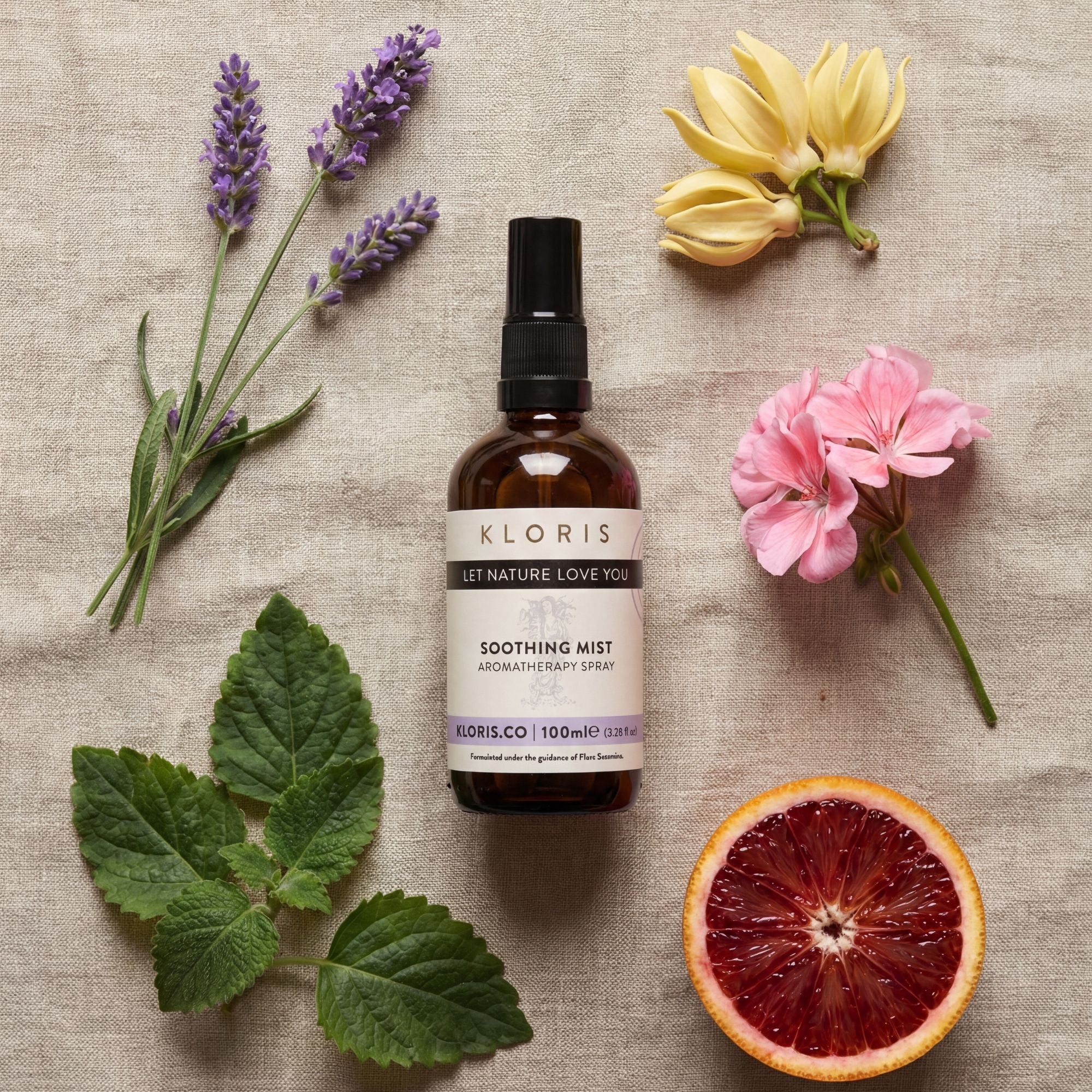 Kloris soothing mist bottle surrounded by flowers and a half blood orange on a textured surface
