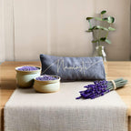 Decorative setting with 'Namaste' pillow, bowls of lavender, and a vase on a wooden surface.