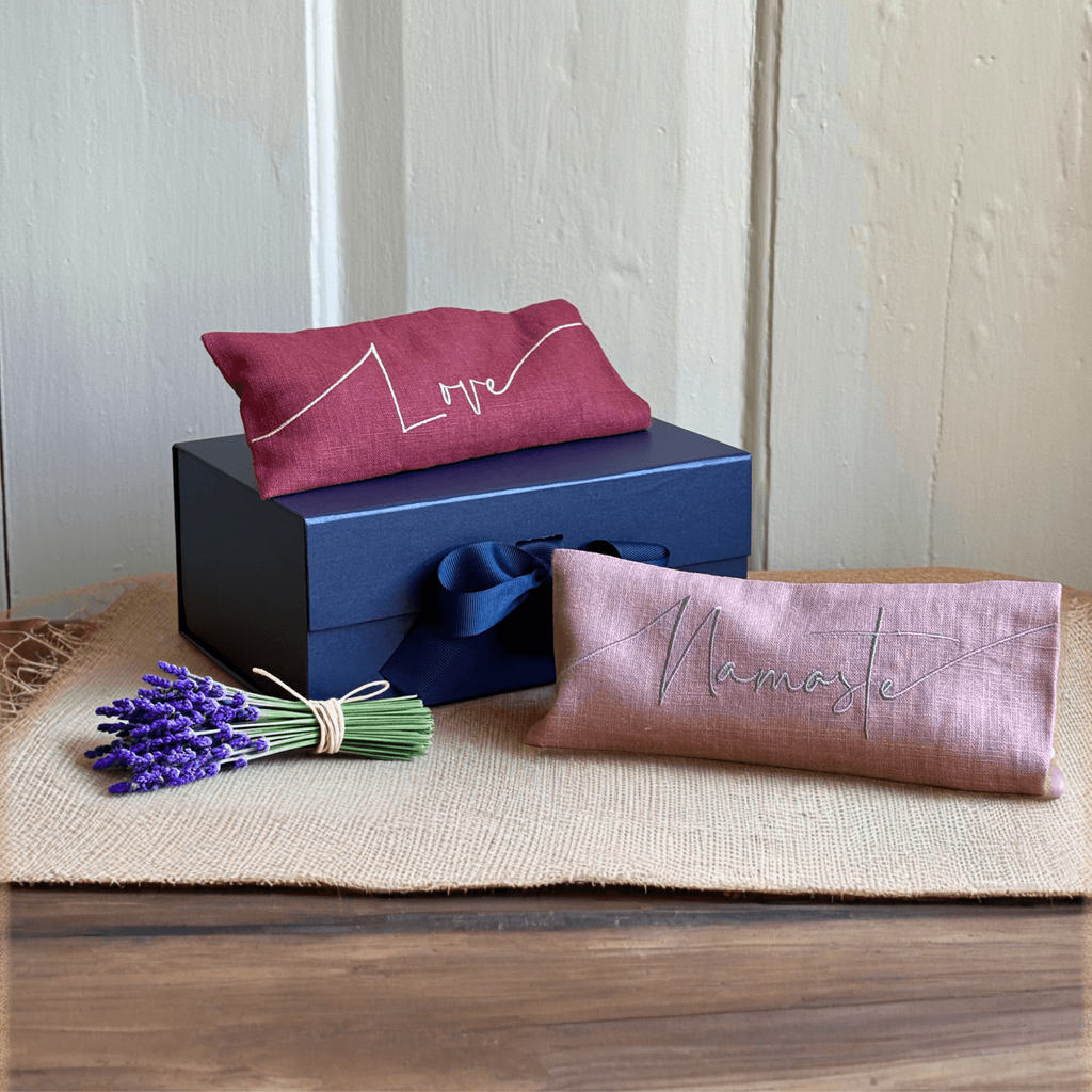 Two embroidered pillows and a blue box on a wooden surface with a lavender bundle.