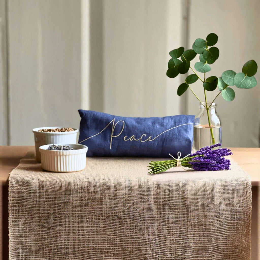 Table setting with a blue pillow, lavender, and eucalyptus on a beige tablecloth.