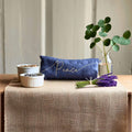 Table setting with a blue pillow, lavender, and eucalyptus on a beige tablecloth.