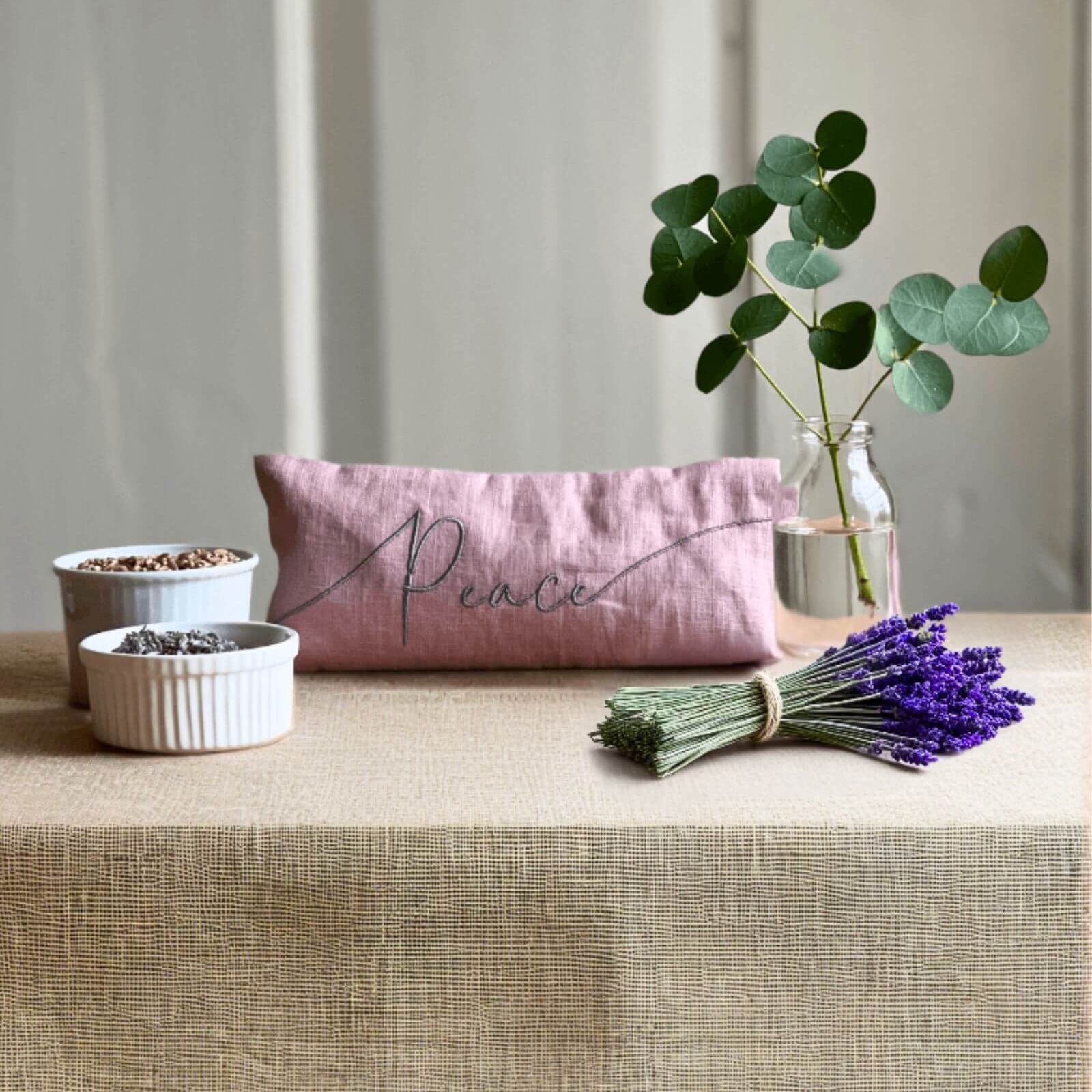 Pink pouch with 'Peace' text on a table with lavender and plants