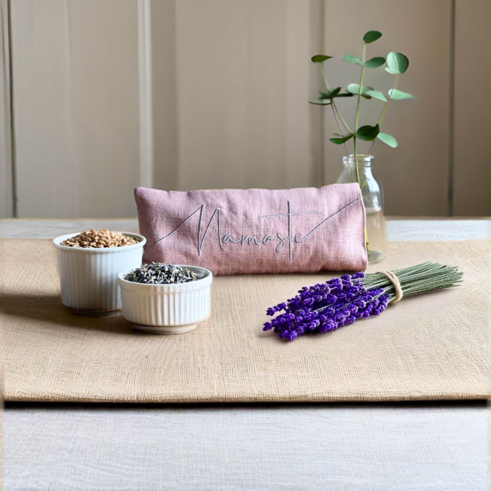 Pink pouch with embroidered text on a table with bowls, lavender, and a plant.