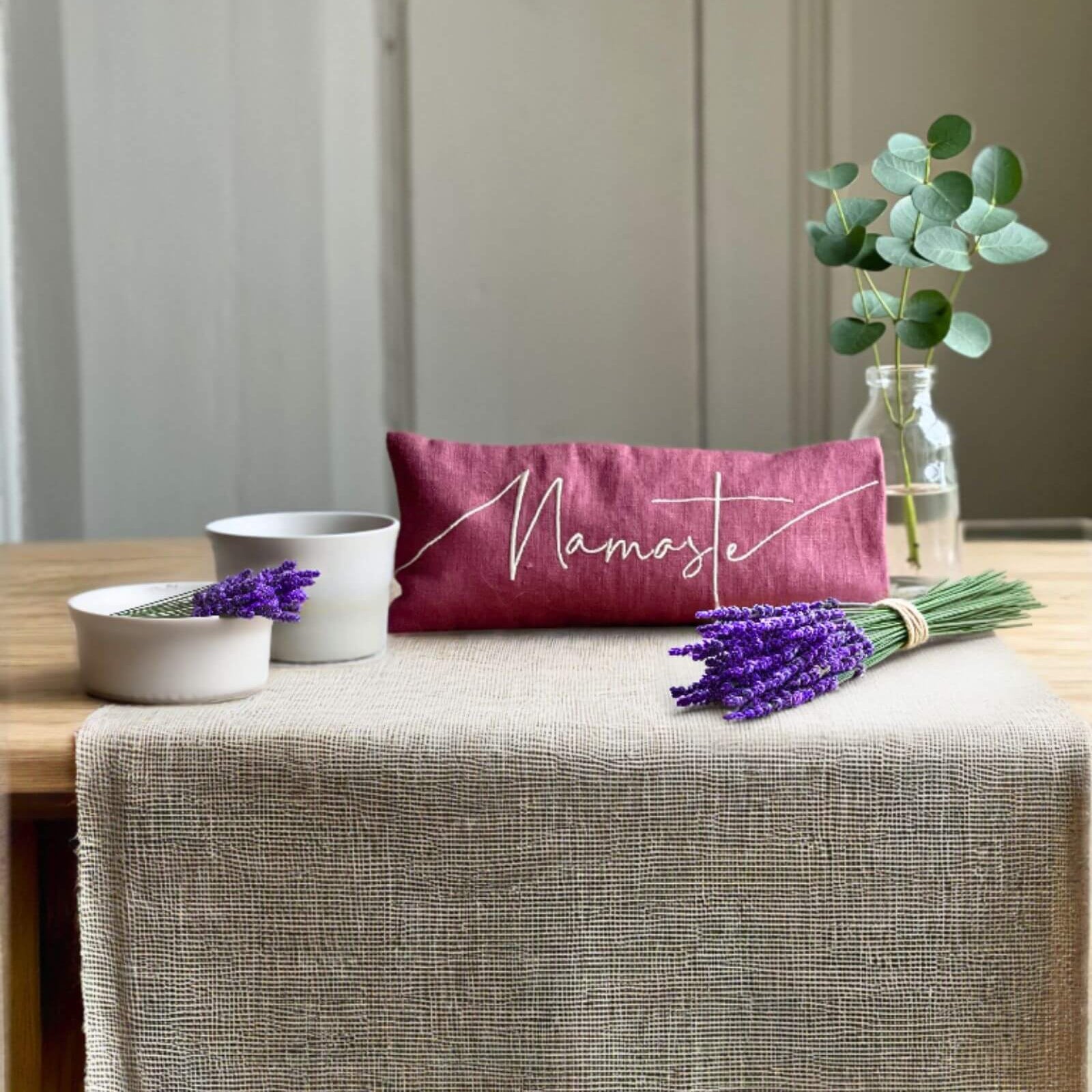 Pink pillow with 'Namaste' text on a table with lavender and a plant.
