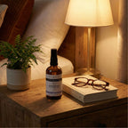 Bottle of Klorane on a wooden nightstand with a book and glasses, next to a lamp and plant.