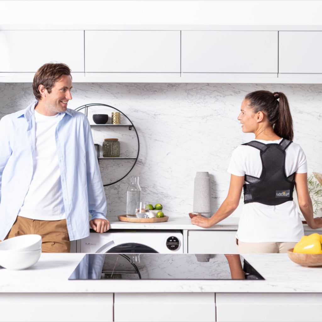 Two people in a kitchen with one wearing a black back brace.