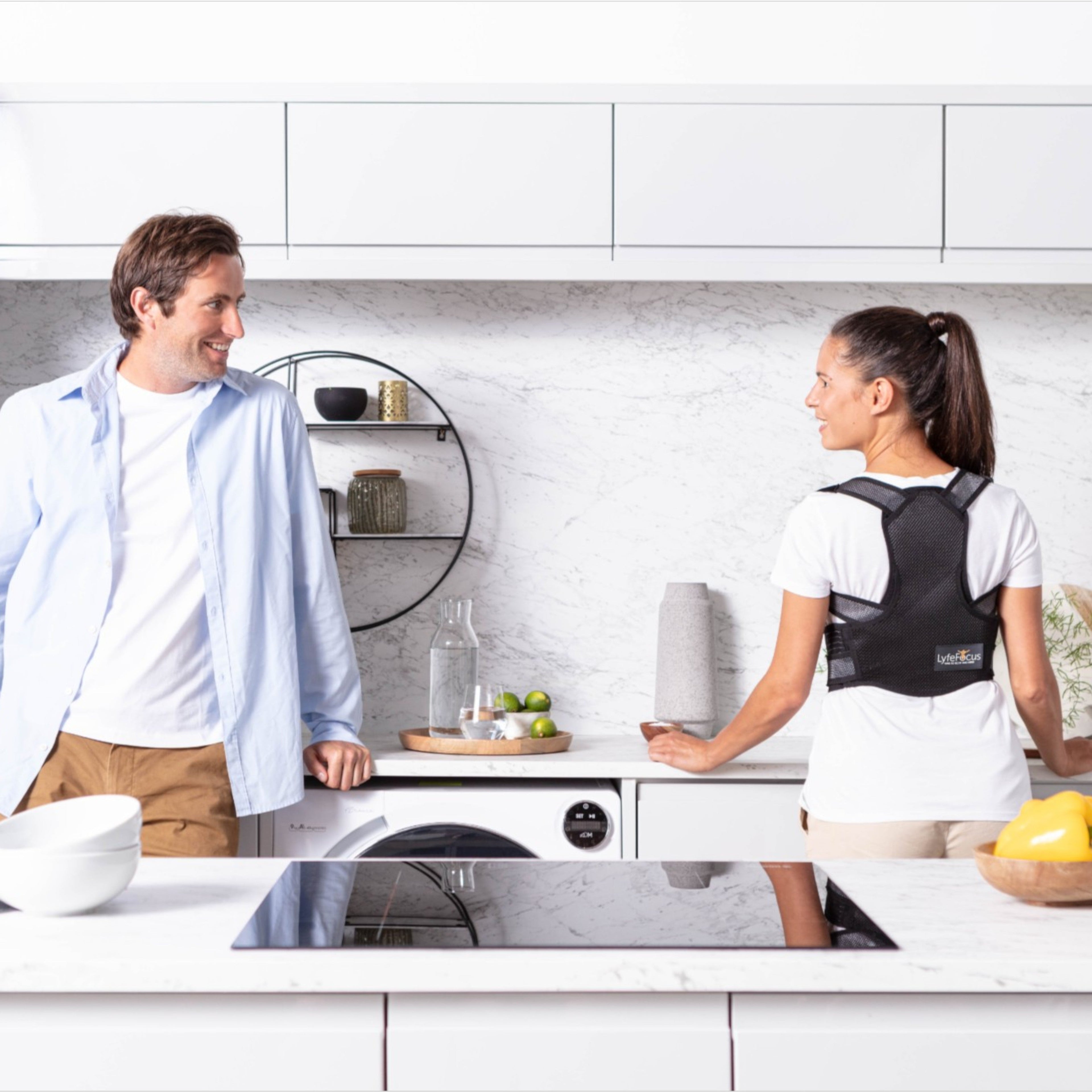 Two people in a kitchen with one wearing a black back brace.