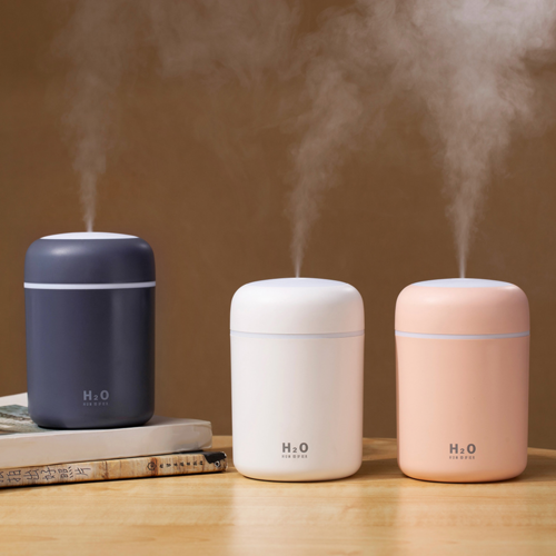 Three humidifiers in blue, white, and pink on a wooden surface with steam rising.