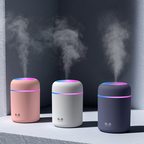 Three humidifiers in pink, white, and black emitting steam on a dark background.