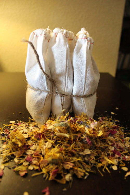 Three white cloth bundles tied together on a bed of dried flowers.
