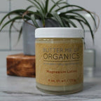 Jar of Butter Me Up Organics magnesium lotion on a marble surface with a plant in the background.