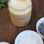 Jar of Butter Me Up Organics magnesium lotion on a wooden surface with ingredients around.