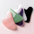 Five gua sha tools in different colors on a light pink background