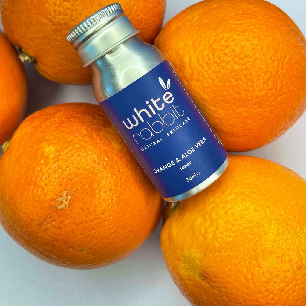 White Rabbit skincare toner bottle surrounded by oranges on a white background