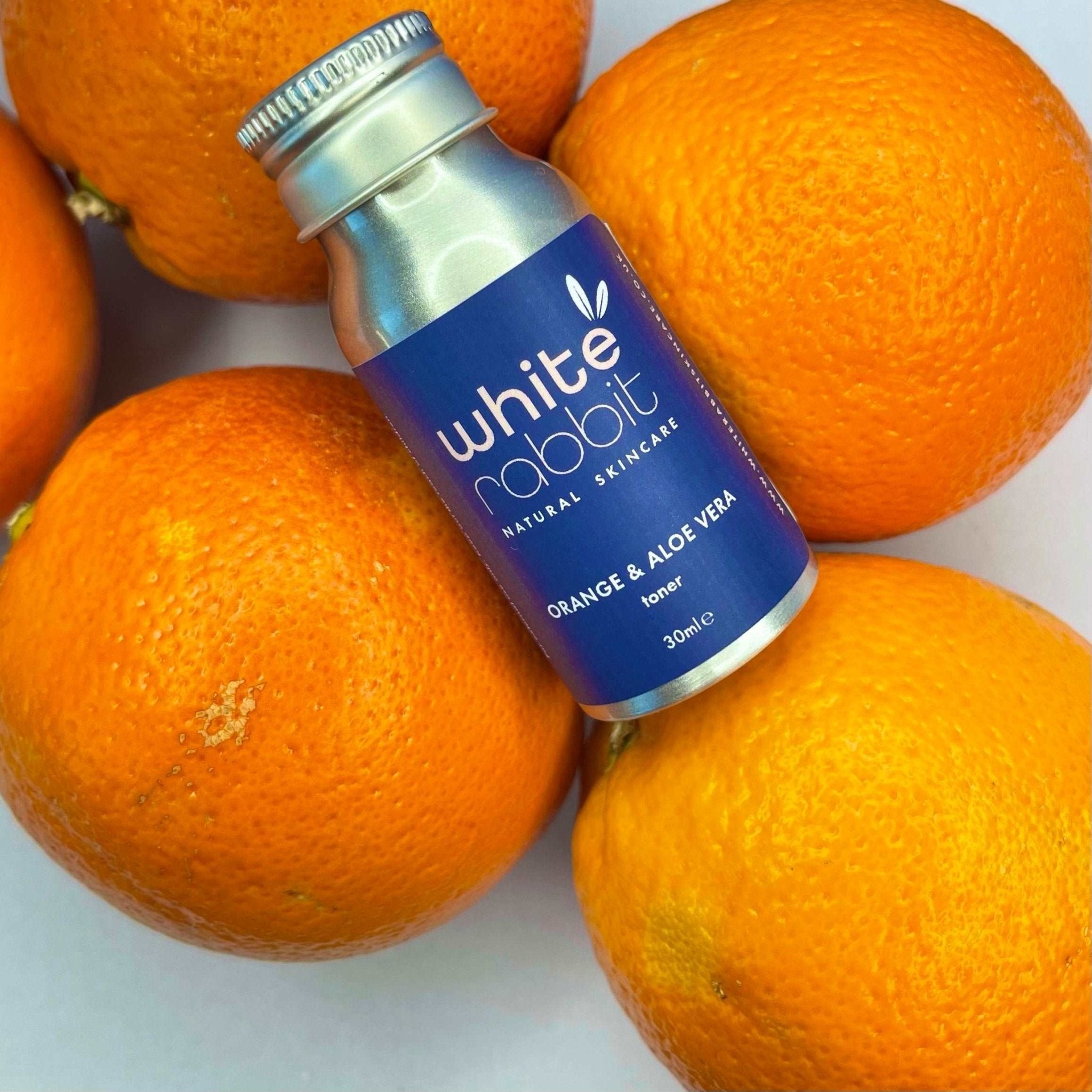White Rabbit skincare toner bottle surrounded by oranges on a white background