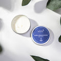 Day cream container with a lit candle on a white background with green leaves.